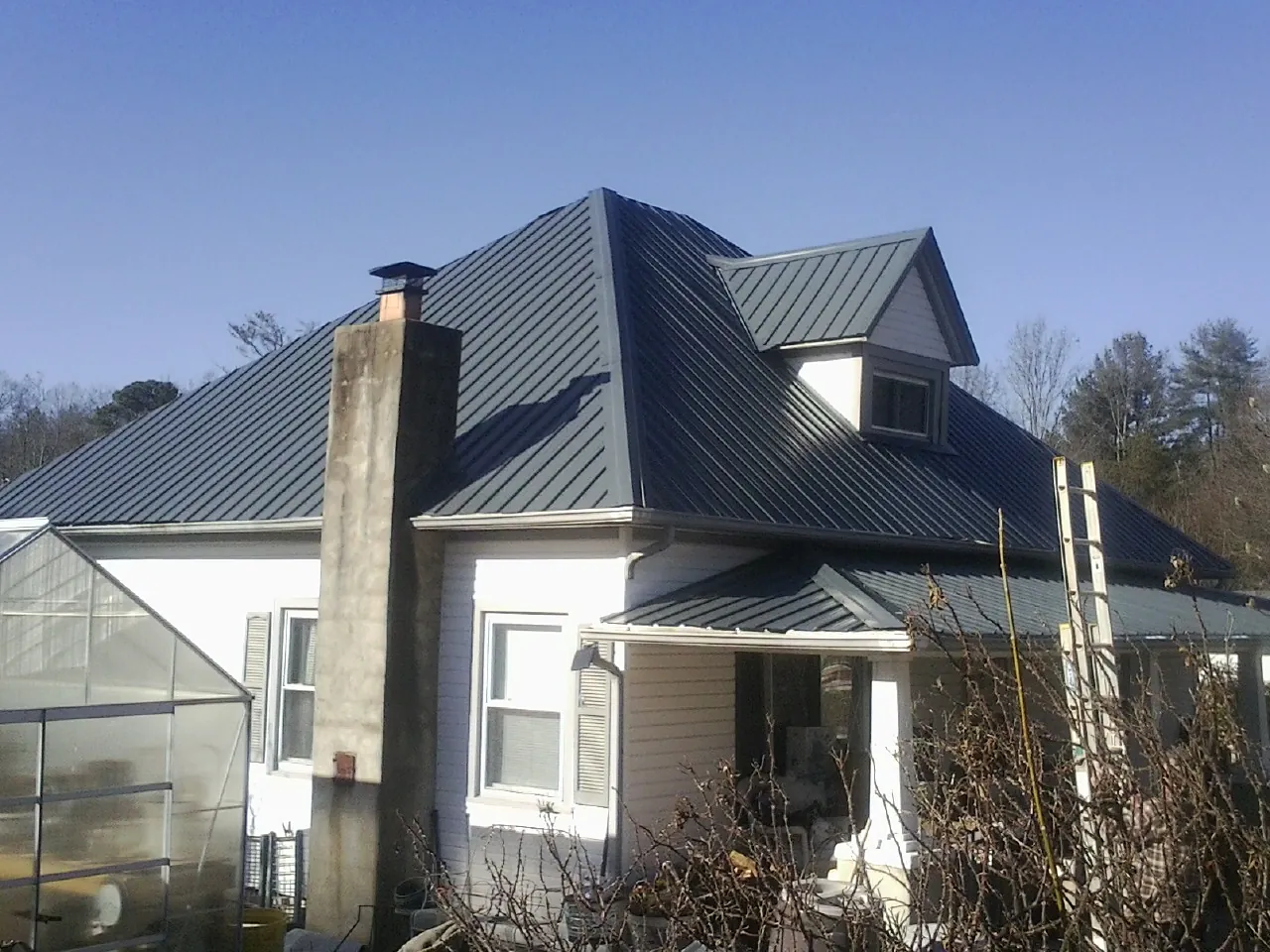 Dark blue standing seam metal roof on a white farmhouse with dormer — Slate & Tile Roof Repair by Roofing Brothers in Pelham
