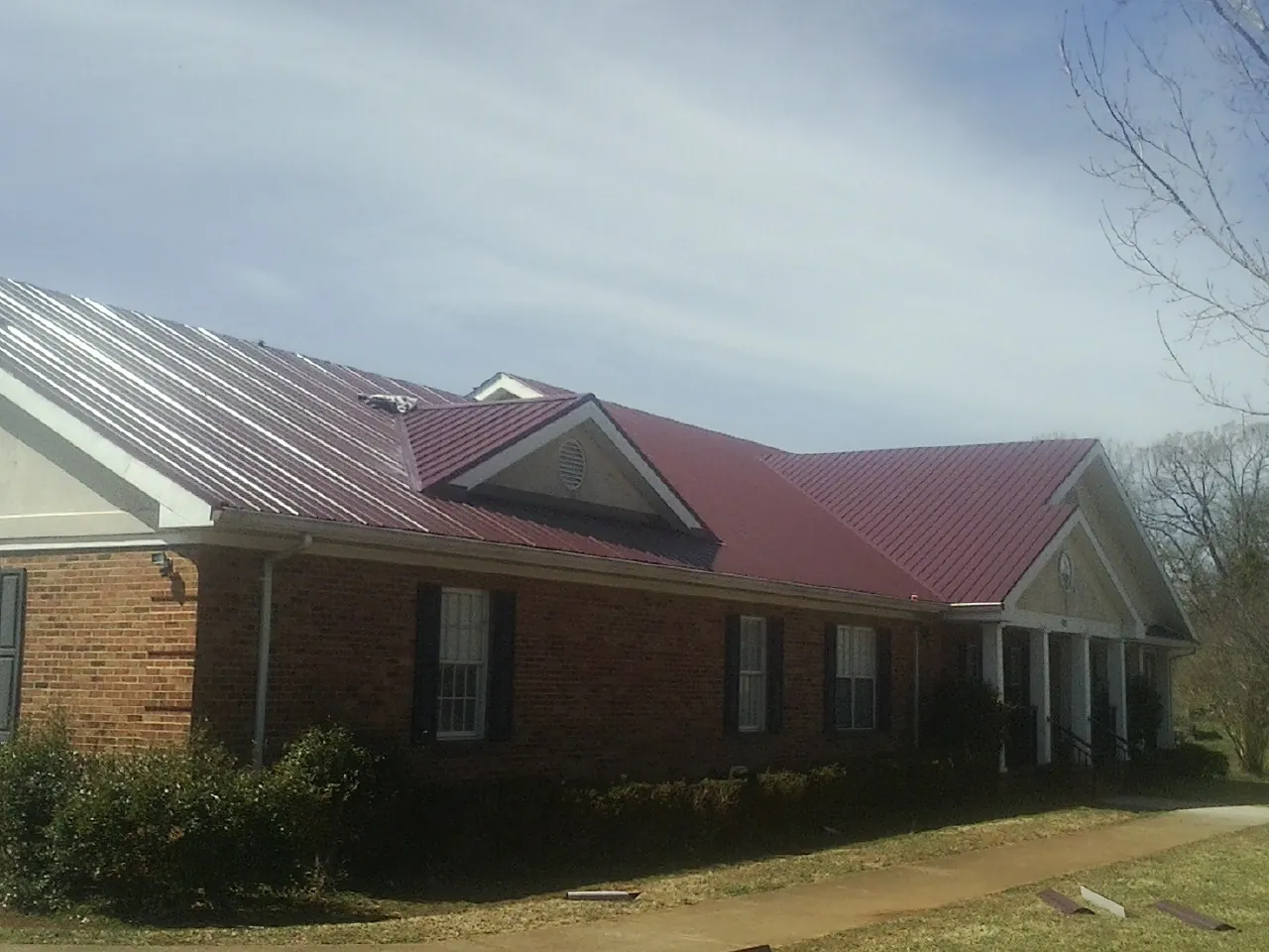 Red metal roof with gabled entries on a long brick building, from a Hail Damage Roof Repair job in Pelham