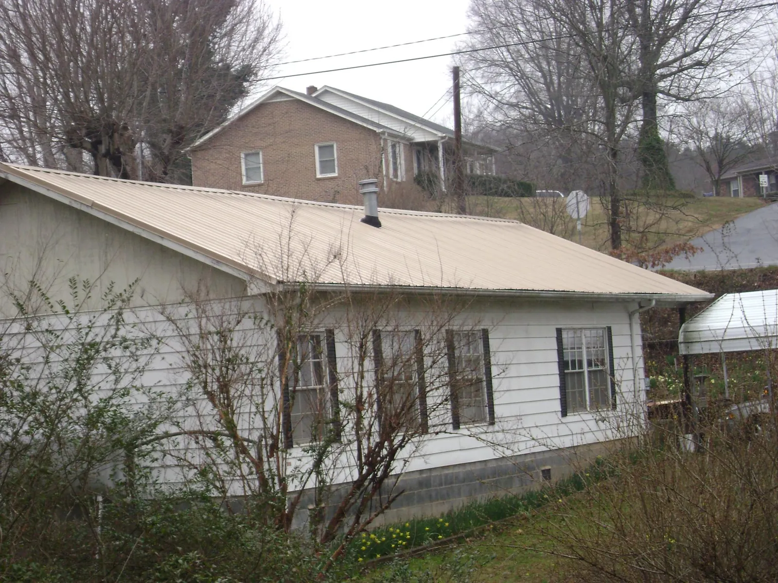 Tan metal roof on a white sided house set into a hillside — Commercial Roofing by Roofing Brothers in Pelham